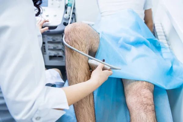 Doctor using ultrasound scanning machine examining injured knee