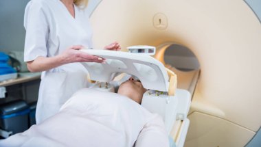 Radyolog genç bayanı MRI beyin muayenesine hazırlıyor.