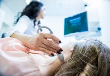 Doktor, bir kadının tiroidini incelemek için ultrason cihazı kullanıyor.