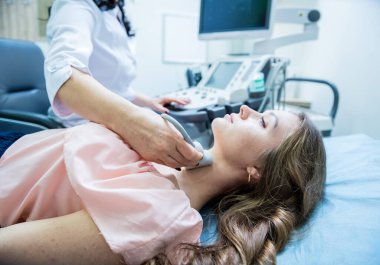Doktor, bir kadının tiroidini incelemek için ultrason cihazı kullanıyor.