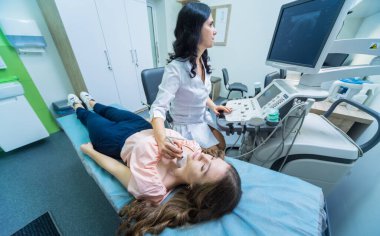 Doktor, bir kadının tiroidini incelemek için ultrason cihazı kullanıyor.