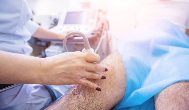 Doktor, yaralı dizleri inceleyen ultrason tarama makinesi kullanıyor.