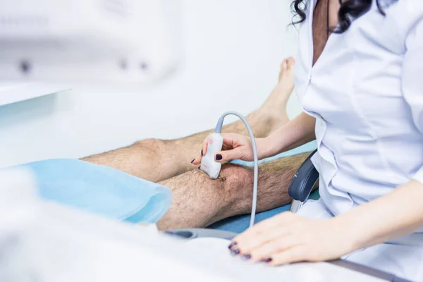 Doctor usando máquina de escaneo de ultrasonido examinando rodilla lesionada — Foto de Stock