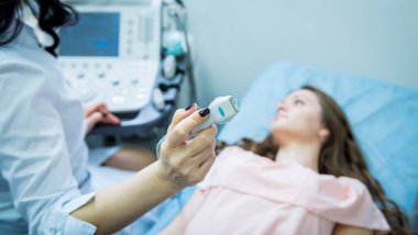 Doktor, bir kadının tiroidini incelemek için ultrason cihazı kullanıyor.