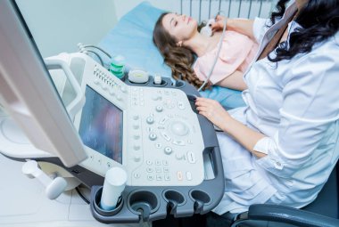 Doktor, bir kadının tiroidini incelemek için ultrason cihazı kullanıyor.