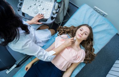 Doktor, bir kadının tiroidini incelemek için ultrason cihazı kullanıyor.