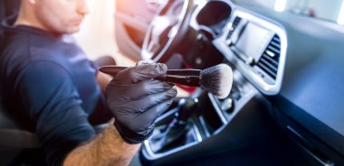 Bir araba servisi çalışanı araba konsolunu özel bir fırçayla temizler.