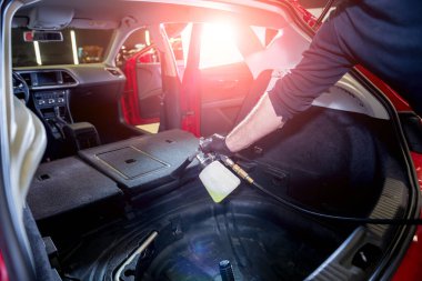 Bir araba servisi çalışanı özel köpük jeneratörüyle iç mekanı temizler.