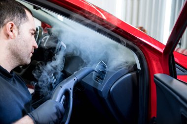 Araba servisi çalışanı iç mekanı buharlı temizleyiciyle temizliyor.