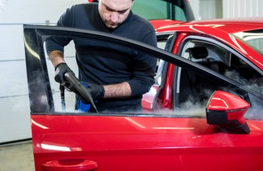 Araba servisi çalışanı iç mekanı buharlı temizleyiciyle temizliyor.