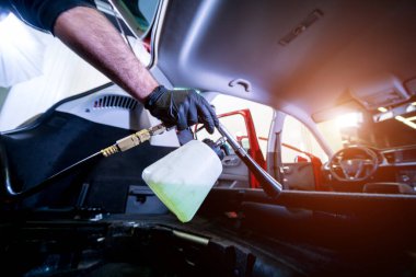 Bir araba servisi çalışanı özel köpük jeneratörüyle iç mekanı temizler.