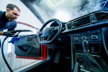 Araba servisi çalışanı araba koltuğunu buharlı temizleme makinesiyle temizliyor.