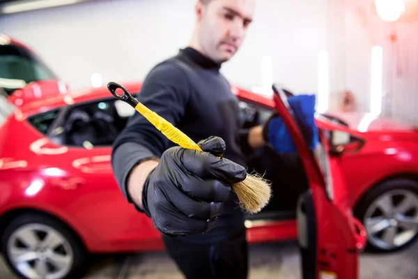 Car service worker cleans interiror with special brush