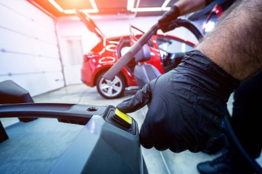 Araba servisi çalışanı elektrikli süpürgeyle araba koltuğunu temizliyor..