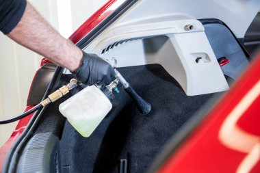 Bir araba servisi çalışanı özel köpük jeneratörüyle iç mekanı temizler.