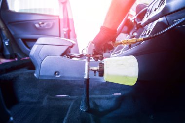 Bir araba servisi çalışanı özel köpük jeneratörüyle iç mekanı temizler.