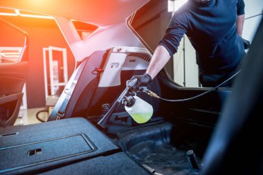 Bir araba servisi çalışanı özel köpük jeneratörüyle iç mekanı temizler.