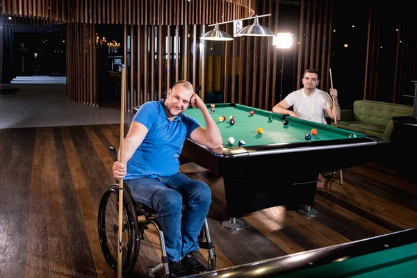 Adult men with disabilities in a wheelchair play billiards in the club