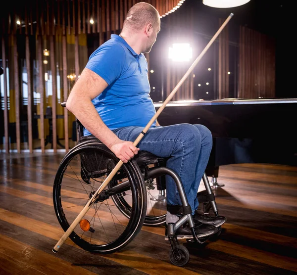 Adult men with disabilities in a wheelchair play billiards in the club