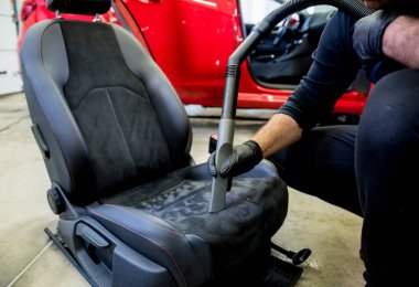 Araba servisi çalışanı elektrikli süpürgeyle araba koltuğunu temizliyor..