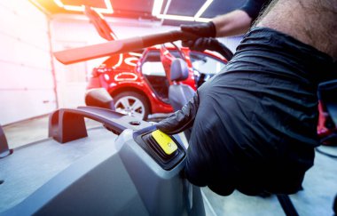 Araba servisi çalışanı elektrikli süpürgeyle araba koltuğunu temizliyor..