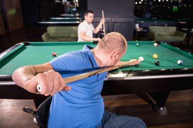 Tekerlekli sandalyedeki engelli yetişkin adamlar kulüpte bilardo oynarlar.