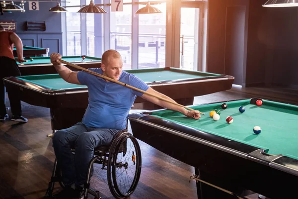 Adult man with disability in a wheelchair play billiards in the club