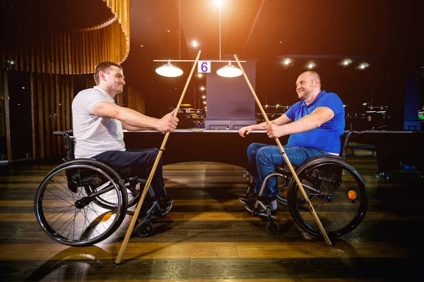 Adult men with disabilities in a wheelchair play billiards in the club