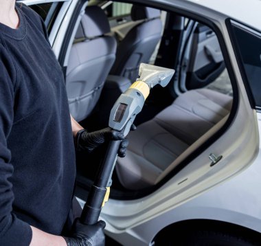 İşçi arabanın içini elektrikli süpürgeyle temizliyor