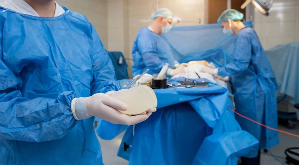 Chirurg na operačním sále drží sterilní prsní silikonový implantát v rukou. — Stock fotografie