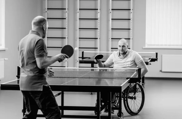 Dorosły niepełnosprawny mężczyzna na wózku inwalidzkim gra w tenisa stołowego ze swoim trenerem — Zdjęcie stockowe