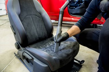 Araba servisi çalışanı elektrikli süpürgeyle araba koltuğunu temizliyor..