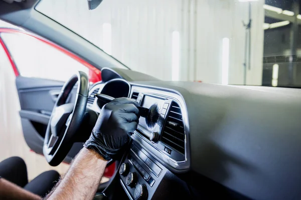 Ein Mitarbeiter des Autoservice reinigt die Fahrzeugkonsole mit einer speziellen Bürste — Stockfoto