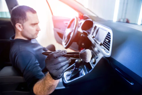 Ein Mitarbeiter des Autoservice reinigt die Fahrzeugkonsole mit einer speziellen Bürste — Stockfoto