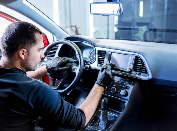 Ein Mitarbeiter des Autoservice reinigt die Fahrzeugkonsole mit einer speziellen Bürste — Stockfoto