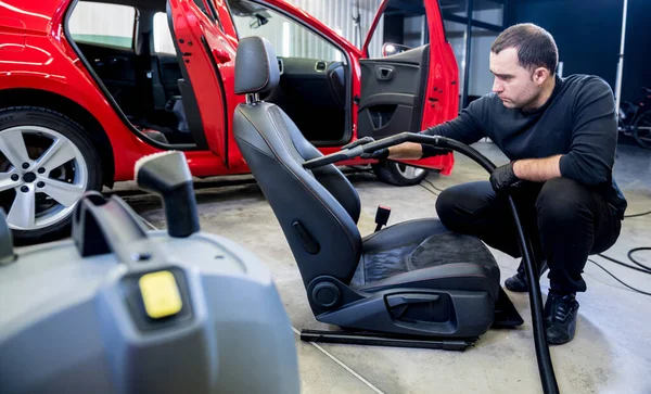 Bilservicearbetare städar bilbarnstol med dammsugare. — Stockfoto