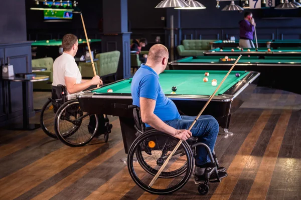 Adult men with disabilities in a wheelchair play billiards in the club