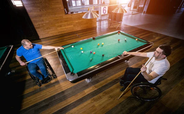 Adult men with disabilities in a wheelchair play billiards in the club