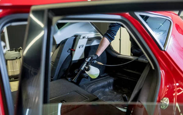 Bir araba servisi çalışanı özel köpük jeneratörüyle iç mekanı temizler.