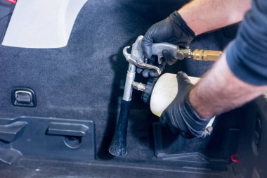 Bir araba servisi çalışanı özel köpük jeneratörüyle iç mekanı temizler.