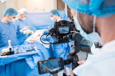 The videographer shoot the surgeon and assistants in the operating room with surgical equipment clipart