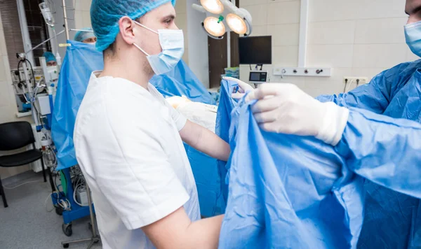Assistant helps the surgeon put on latex gloves and surgical gown before the operation.