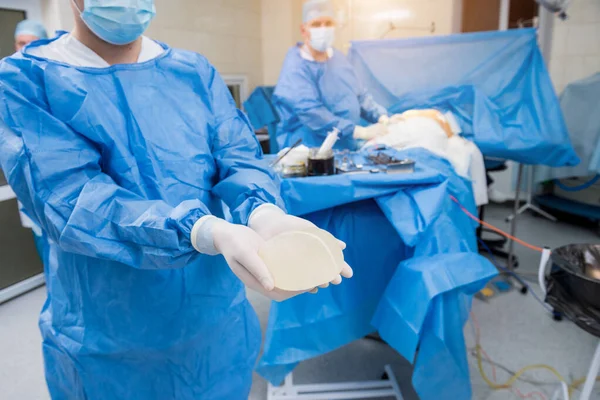 Chirurg w sali operacyjnej trzyma sterylny implant silikonowy w rękach. — Zdjęcie stockowe