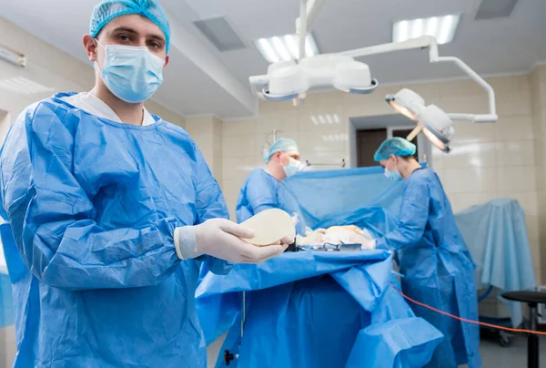 Хирург в операционной держит в руках стерильный силиконовый имплантат груди. — стоковое фото