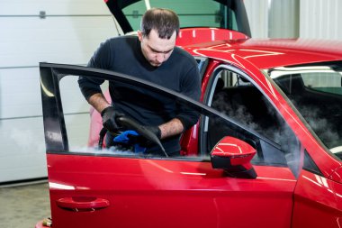 Araba servisi çalışanı iç mekanı buharlı temizleyiciyle temizliyor.