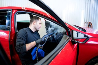 Araba servisi çalışanı iç mekanı buharlı temizleyiciyle temizliyor.