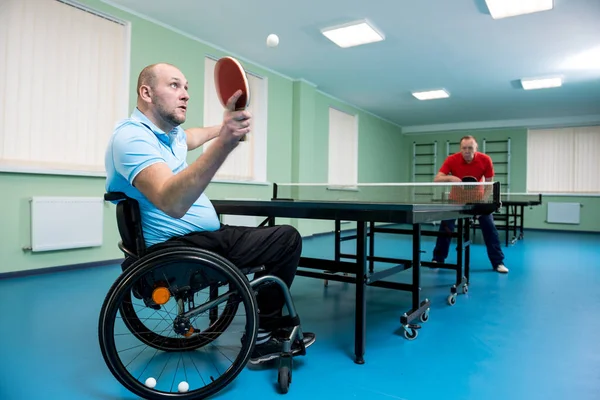 Взрослый инвалид в инвалидной коляске играет в настольный теннис со своим тренером — стоковое фото