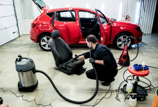 Autószerelő porszívóval tisztítja az autóülést. — Stock Fotó
