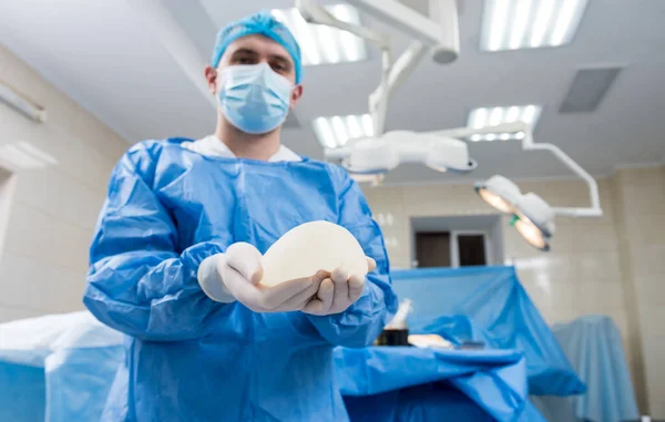Cirurgião em sala de operação está segurando implante de silicone estéril mama nas mãos. — Fotografia de Stock
