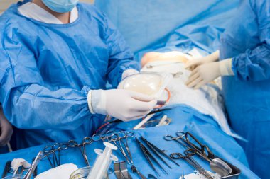 Ameliyathanedeki cerrah steril göğüs silikonu elinde tutuyor..